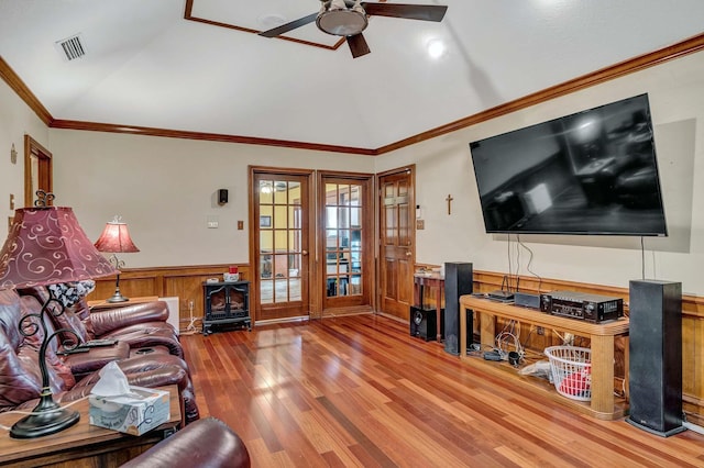 living area featuring lofted ceiling, a wainscoted wall, wood finished floors, visible vents, and ornamental molding