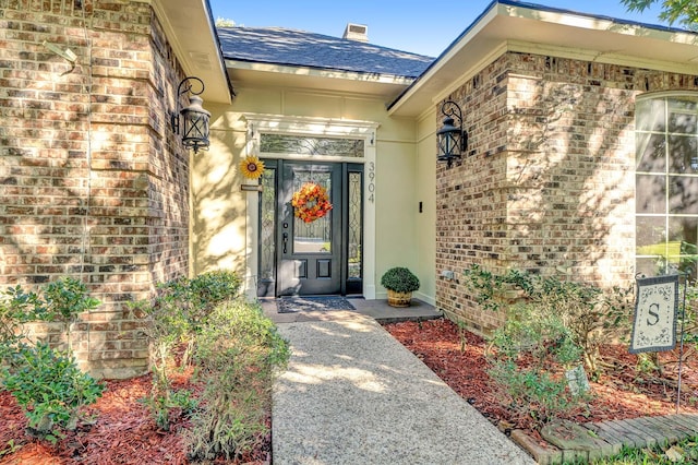 view of exterior entry with brick siding and a shingled roof