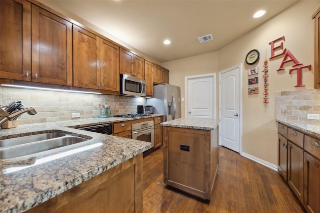 kitchen with dark wood-type flooring, sink, light stone counters, a kitchen island, and stainless steel appliances