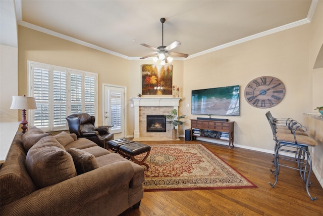 living room with ornamental molding, wood-type flooring, a tile fireplace, and ceiling fan