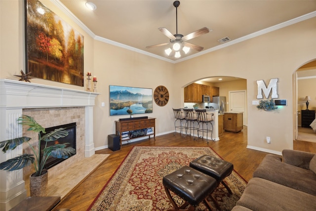 living room with ceiling fan, ornamental molding, a fireplace, and hardwood / wood-style floors