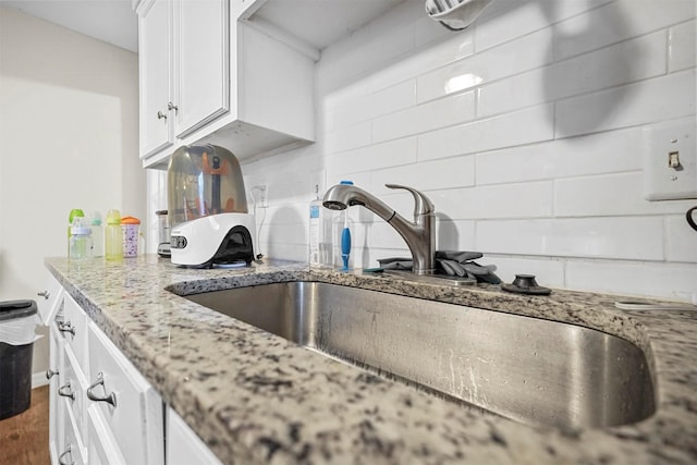 kitchen featuring white cabinetry, light stone countertops, sink, and backsplash