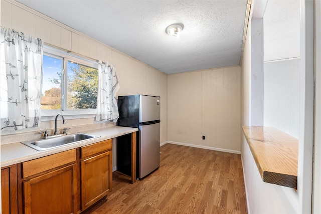 kitchen featuring stainless steel fridge, light hardwood / wood-style floors, sink, and a textured ceiling