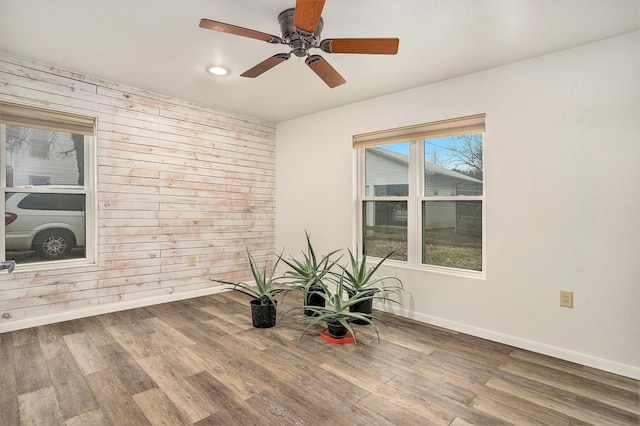 empty room featuring ceiling fan, wood-type flooring, and wood walls