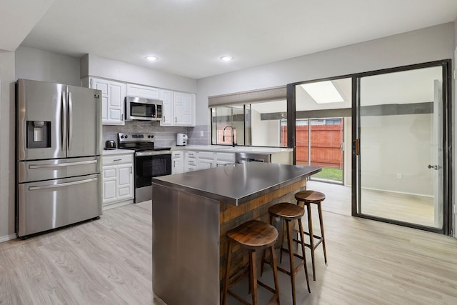 kitchen featuring tasteful backsplash, a kitchen breakfast bar, stainless steel appliances, light hardwood / wood-style floors, and white cabinets