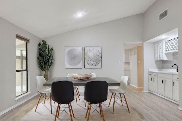 dining space featuring a healthy amount of sunlight, lofted ceiling, sink, and light hardwood / wood-style floors