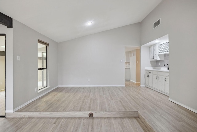 unfurnished living room featuring lofted ceiling, sink, and light hardwood / wood-style floors