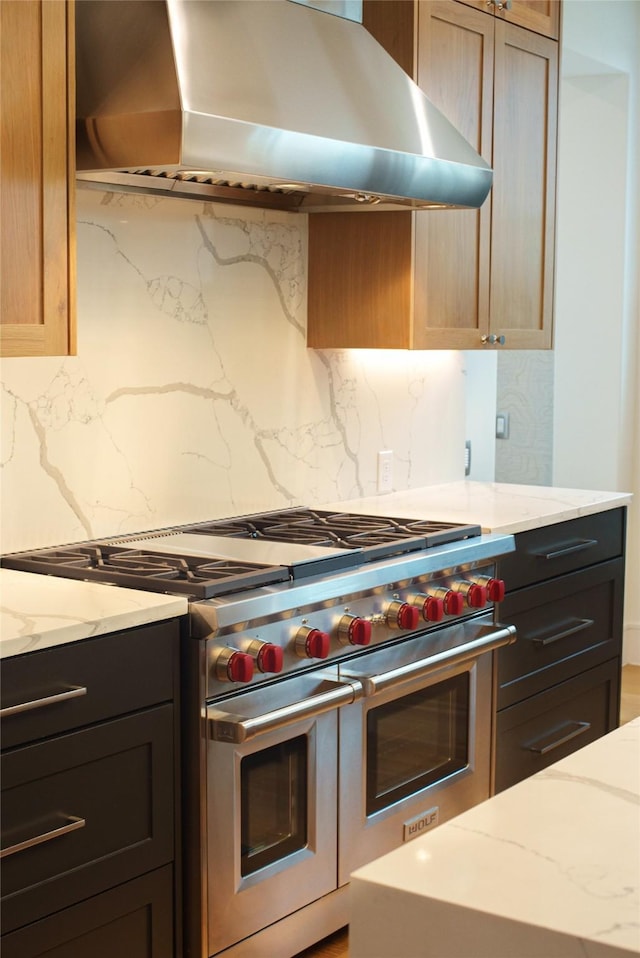 kitchen featuring wall chimney exhaust hood, double oven range, light stone countertops, and decorative backsplash