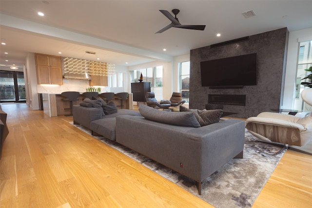 living room featuring light wood-type flooring, visible vents, recessed lighting, a ceiling fan, and a large fireplace
