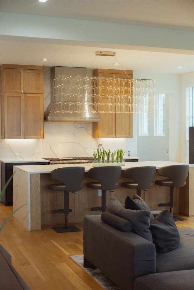 interior space with wall chimney range hood, backsplash, a kitchen bar, and light hardwood / wood-style floors