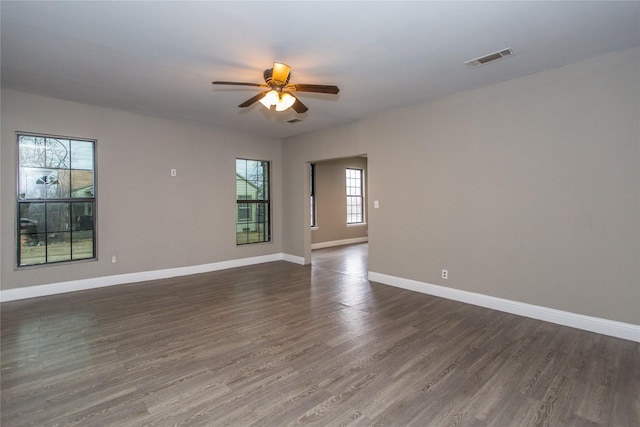 empty room featuring ceiling fan, dark wood-type flooring, visible vents, and baseboards