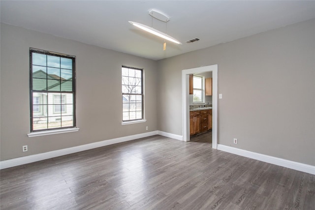 spare room with dark wood-type flooring, a sink, visible vents, and baseboards