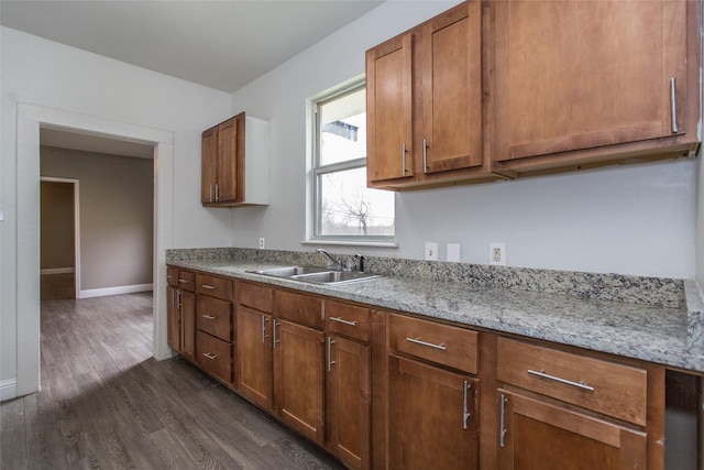 kitchen featuring dark wood-style floors, a sink, light stone countertops, and brown cabinets