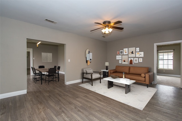 living area with a ceiling fan, visible vents, baseboards, and wood finished floors