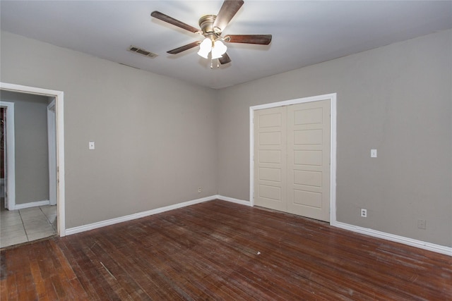 unfurnished room featuring ceiling fan, visible vents, dark wood finished floors, and baseboards