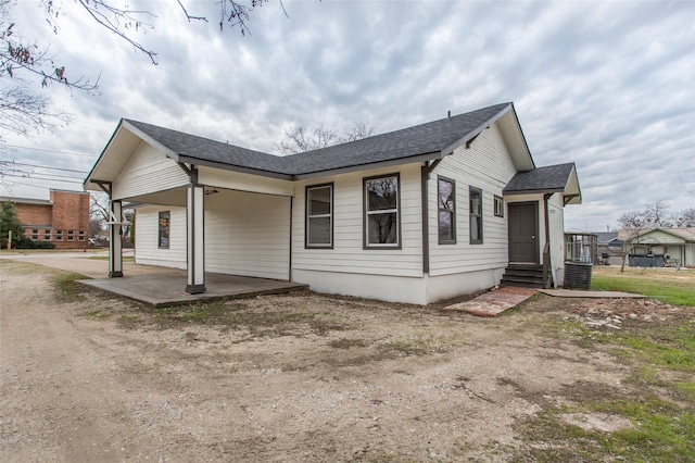 view of side of home featuring a shingled roof, entry steps, and a patio