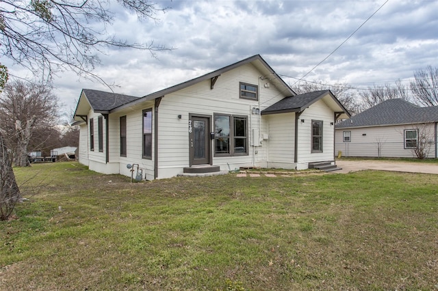 bungalow-style house with entry steps, roof with shingles, and a front yard