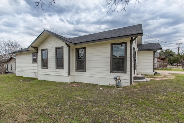 view of side of home with roof with shingles and a lawn