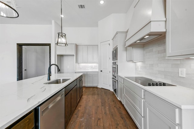 kitchen featuring premium range hood, sink, decorative light fixtures, appliances with stainless steel finishes, and light stone countertops