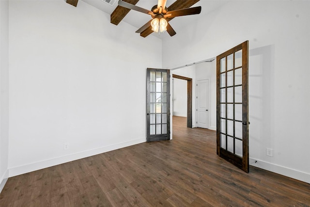 empty room featuring ceiling fan, dark wood-type flooring, beam ceiling, and a towering ceiling