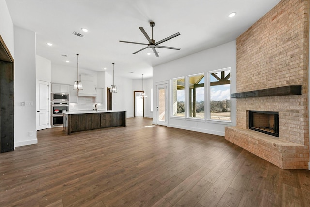 unfurnished living room with ceiling fan, dark hardwood / wood-style floors, sink, and a brick fireplace