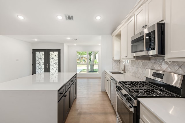 kitchen with sink, white cabinets, decorative backsplash, stainless steel appliances, and light wood-type flooring