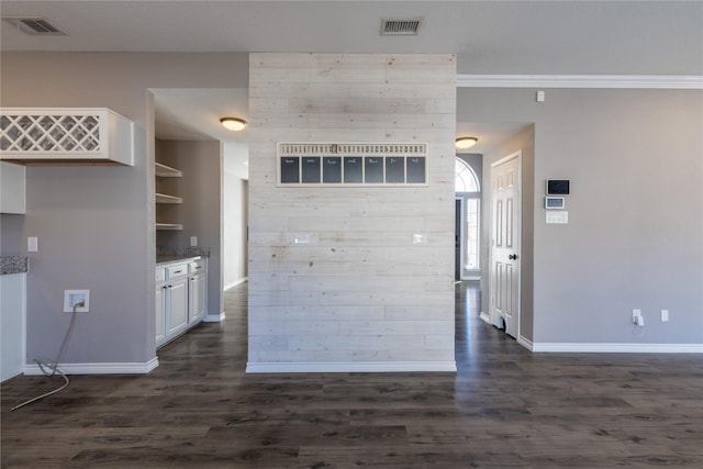 kitchen with dark wood-type flooring, light stone counters, white cabinets, and wooden walls