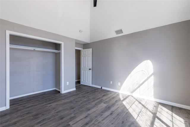 unfurnished bedroom with a closet, dark hardwood / wood-style floors, and a high ceiling