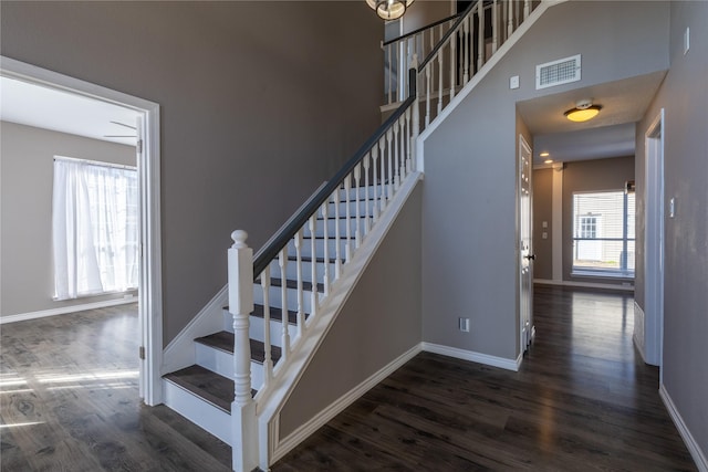 stairs with a towering ceiling, wood-type flooring, and a healthy amount of sunlight