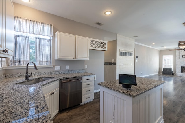 kitchen with sink, light stone counters, stainless steel dishwasher, a large fireplace, and white cabinets