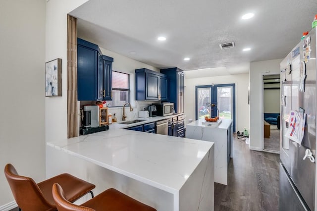 kitchen with sink, blue cabinetry, appliances with stainless steel finishes, dark hardwood / wood-style flooring, and kitchen peninsula