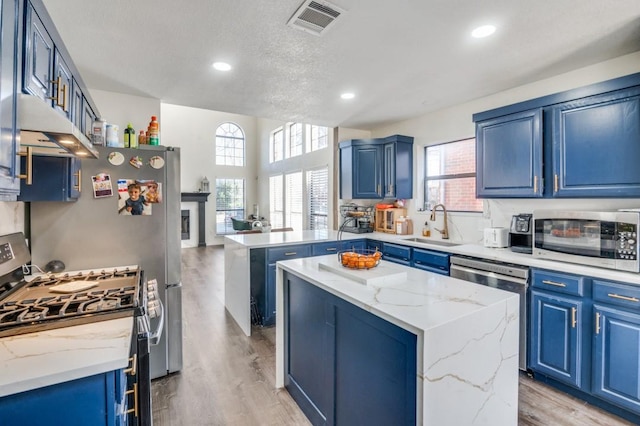 kitchen with blue cabinets, a kitchen island, appliances with stainless steel finishes, and light stone counters