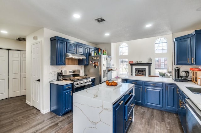 kitchen featuring appliances with stainless steel finishes, dark hardwood / wood-style flooring, a center island, light stone countertops, and blue cabinetry