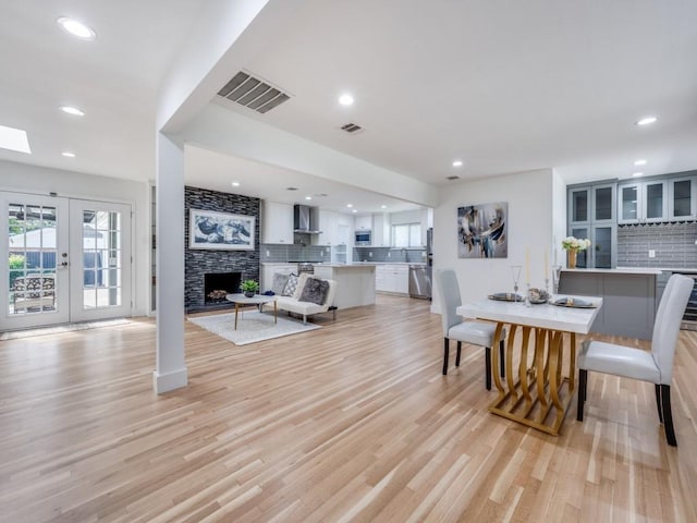 dining room featuring a healthy amount of sunlight, a fireplace, light hardwood / wood-style floors, and french doors