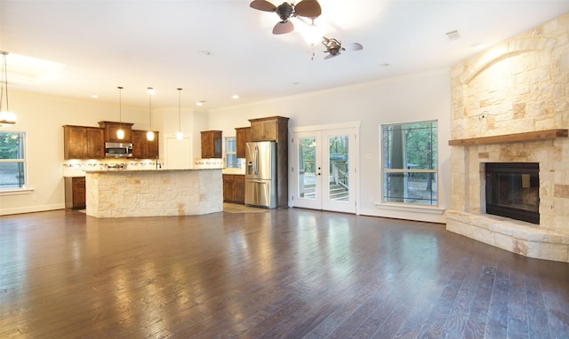 unfurnished living room featuring french doors, ornamental molding, dark hardwood / wood-style floors, ceiling fan, and a fireplace