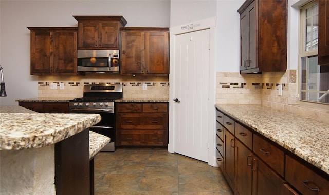 kitchen featuring stainless steel appliances, light stone countertops, backsplash, and dark brown cabinetry