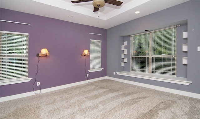 carpeted spare room with a raised ceiling and ceiling fan