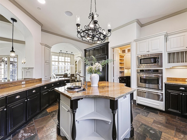 kitchen with white cabinetry, stainless steel appliances, hanging light fixtures, and a center island with sink