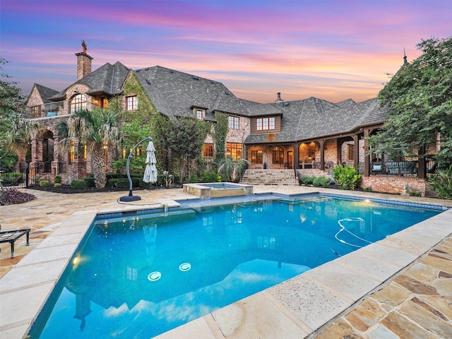 pool at dusk featuring an in ground hot tub and a patio area