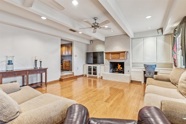 living room with ceiling fan, a fireplace, beam ceiling, and light hardwood / wood-style flooring