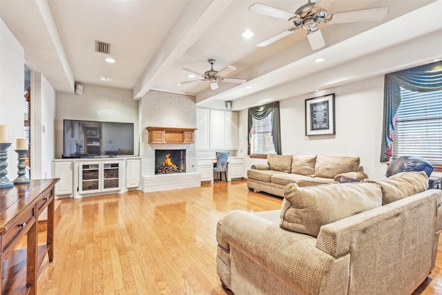 living room with beamed ceiling, a fireplace, and light hardwood / wood-style flooring