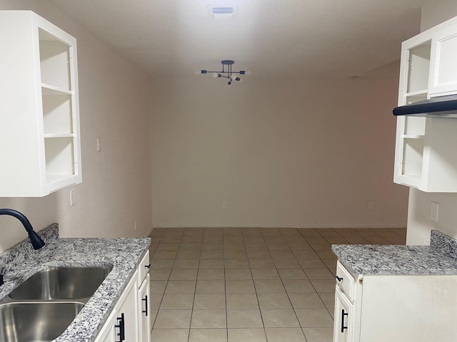 kitchen with light stone countertops, sink, light tile patterned floors, and white cabinets