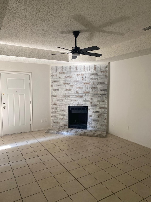 unfurnished living room featuring ceiling fan, a fireplace, a textured ceiling, and light tile patterned floors