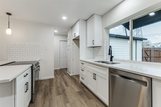 kitchen with sink, appliances with stainless steel finishes, decorative backsplash, white cabinets, and decorative light fixtures