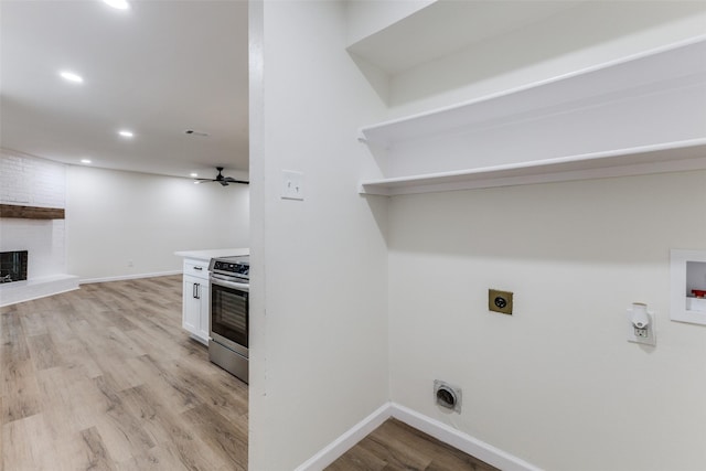 clothes washing area with electric dryer hookup, washer hookup, a fireplace, hookup for a gas dryer, and light hardwood / wood-style floors