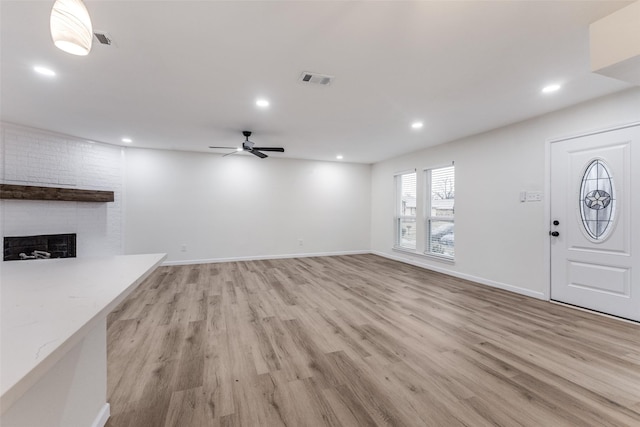 unfurnished living room with a brick fireplace, ceiling fan, and light hardwood / wood-style flooring