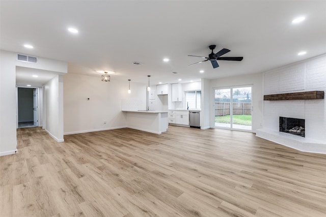 unfurnished living room featuring ceiling fan, a brick fireplace, and light wood-type flooring