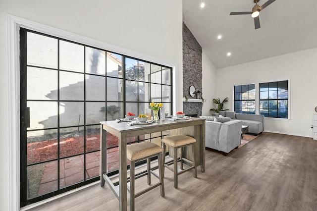 dining space featuring ceiling fan, hardwood / wood-style floors, a fireplace, and high vaulted ceiling