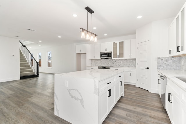 kitchen with white cabinetry, a center island, appliances with stainless steel finishes, pendant lighting, and light stone countertops