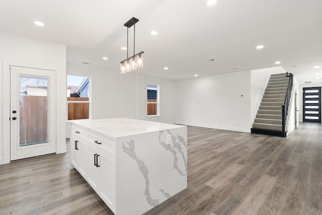 kitchen featuring dark wood-type flooring, light stone counters, a center island, hanging light fixtures, and white cabinets